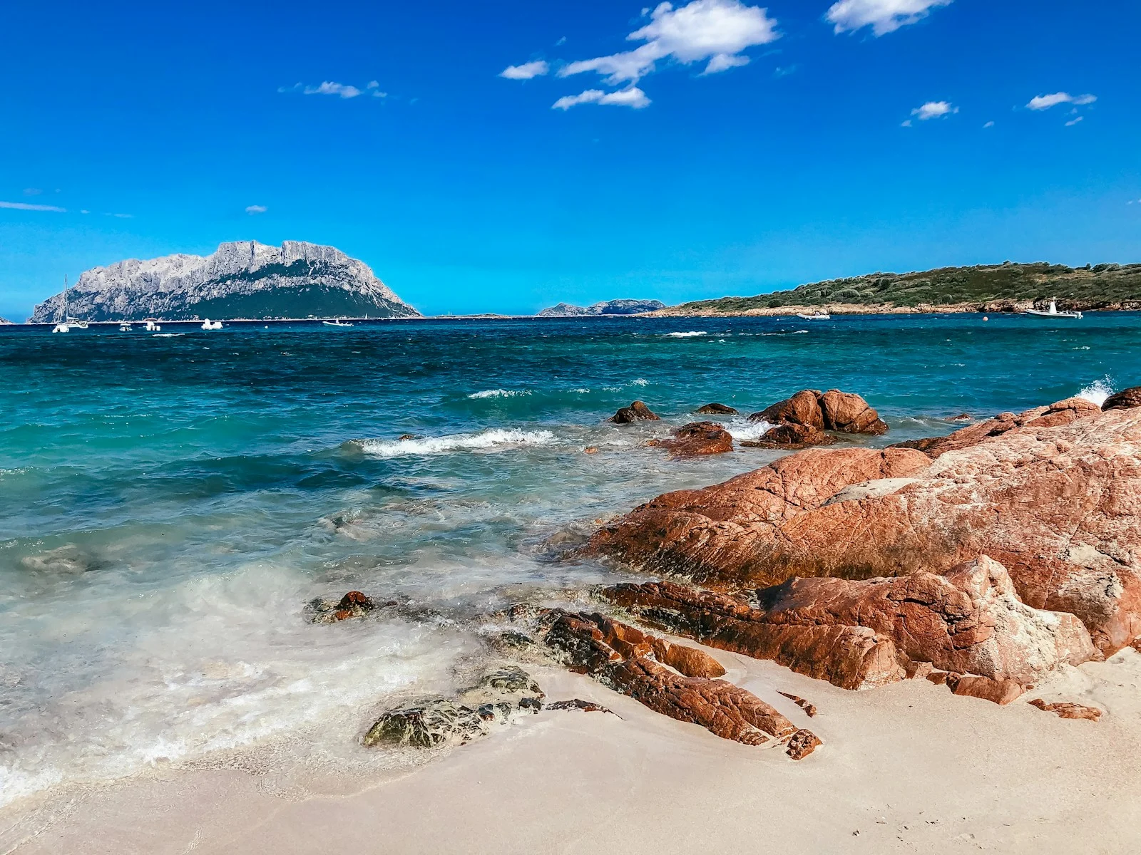 a rocky beach with clear blue water and a mountain in the distance